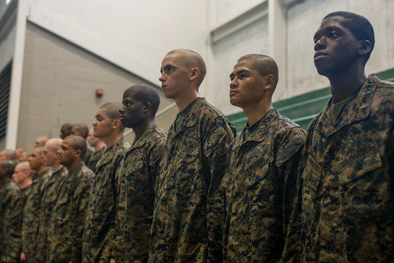 Marines in camouflage stand in a row, facing forward, each with a serious look.