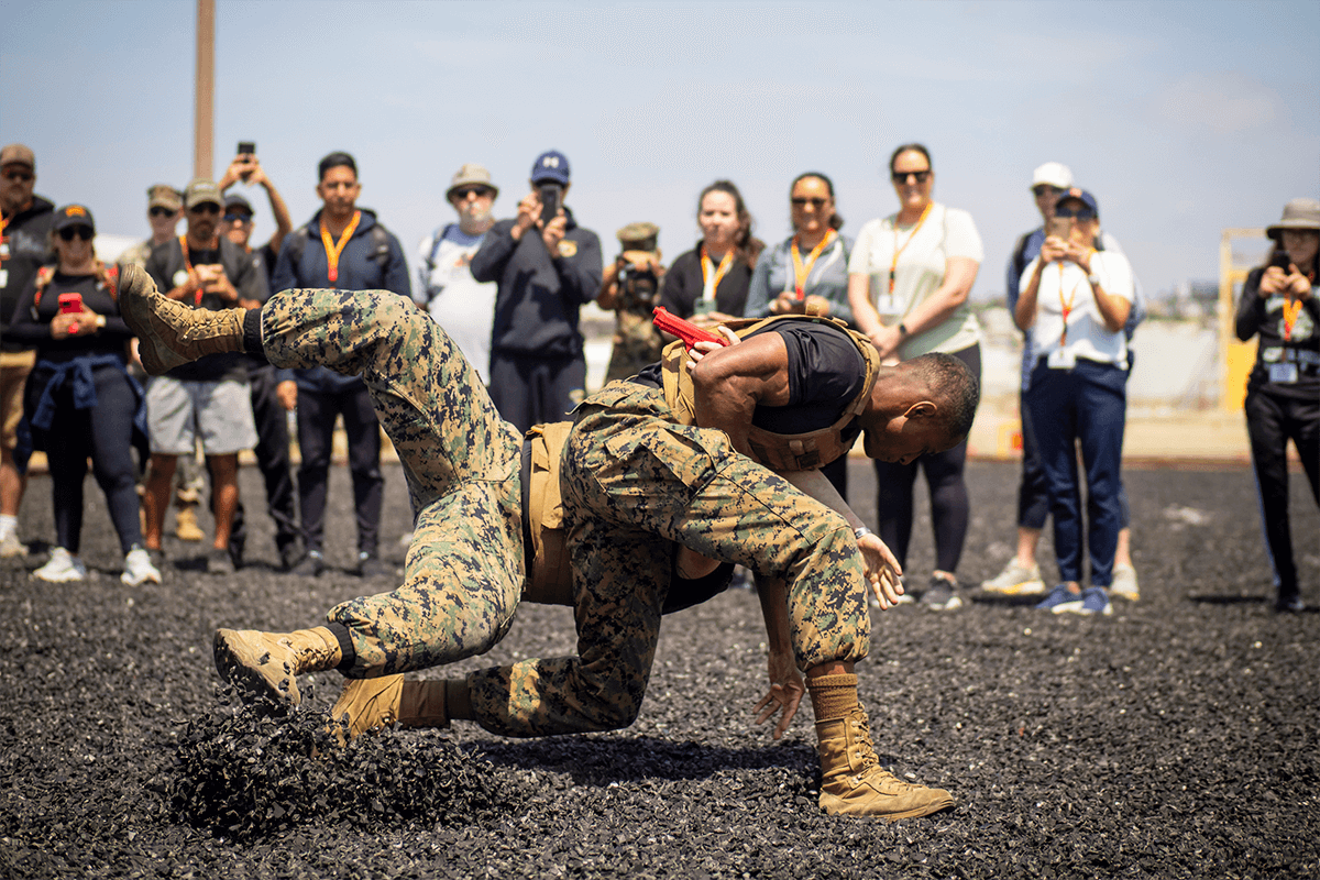 Two Marines in utility uniforms demonstrate martial arts for a group of teachers and coaches.