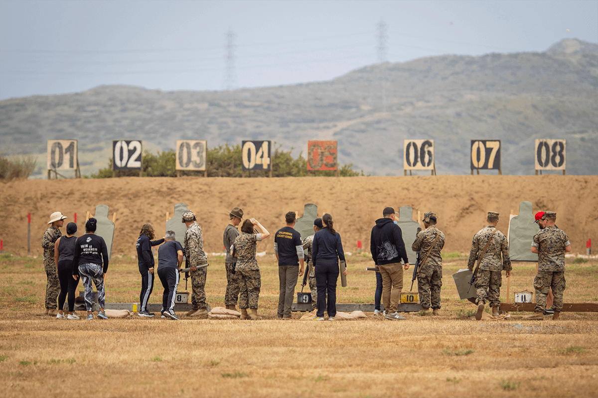 Educators receive instruction from Marines at an outdoors rifle range.
