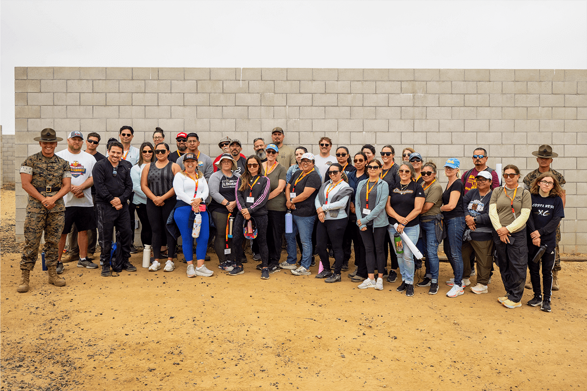 A large group of smiling educators pose with Marine corps drill instructors in front of a concrete wall.