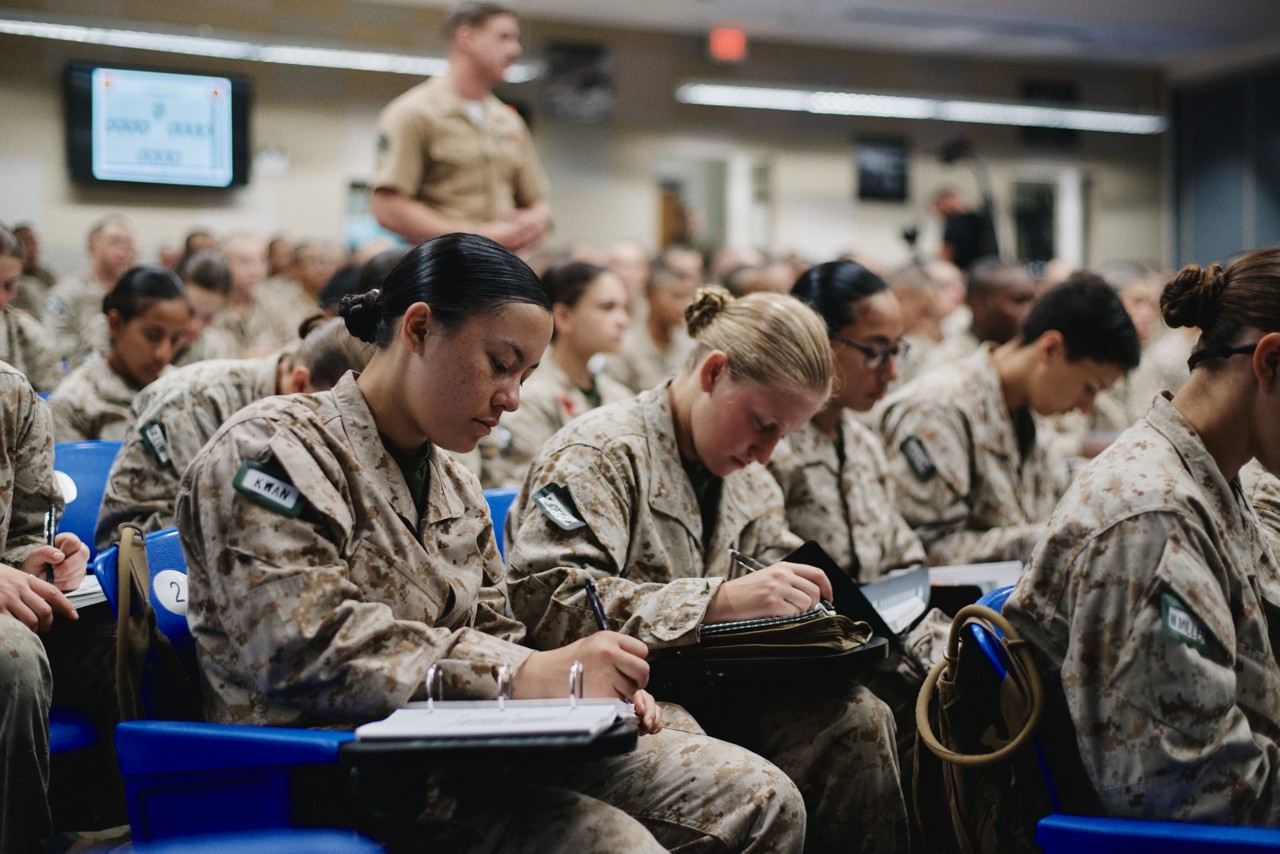 Marines sit in a classroom collectively learning from a higher rank Marine. 