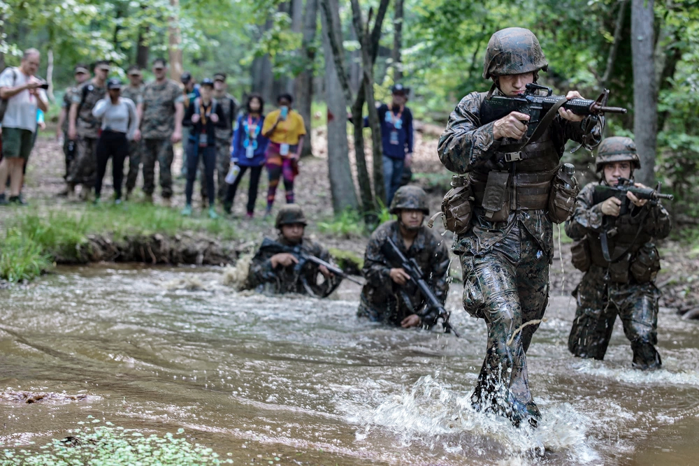 Educators observe a group of Marines demonstrate a training exercise in a wooded area.