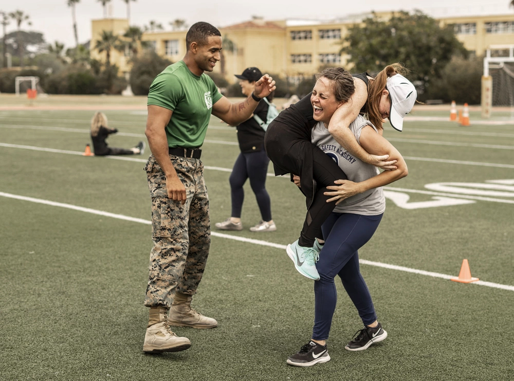 A Marine motivates two educators participating in the combat fitness test.