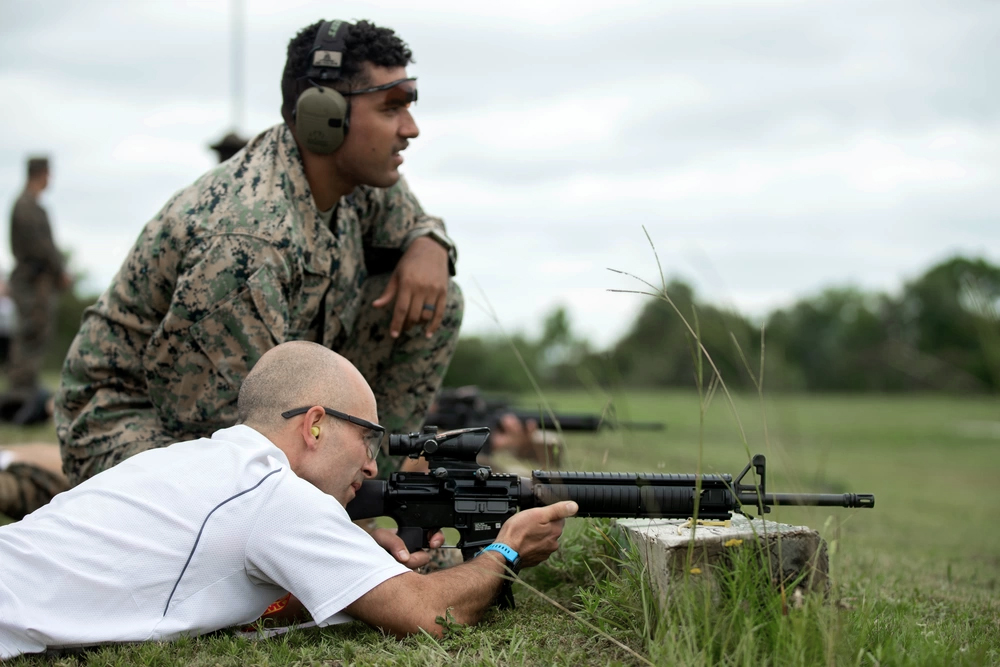 A young, male Marine assists an educator on the shooting range.