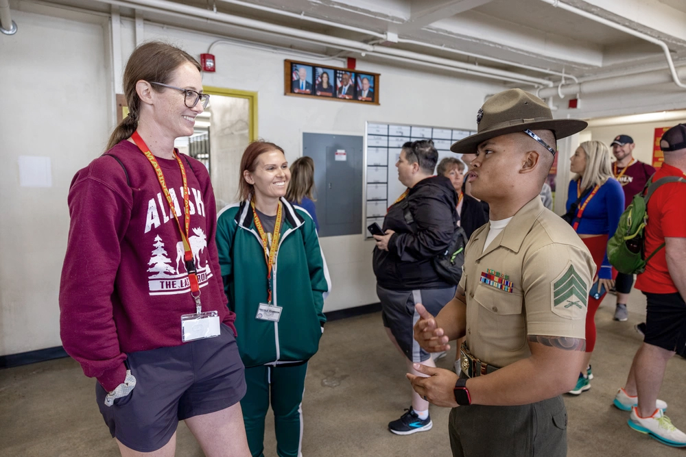 Two smiling educators speak with a Marien Drill Instructor in a classroom.